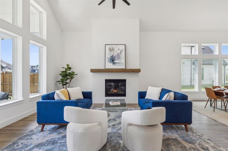 Living room featuring wood-type flooring, a tiled fireplace, a towering ceiling, and ceiling fan