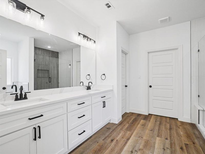 Bathroom featuring double vanity, a stall shower, and dark wood-type flooring