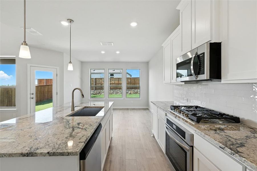 Kitchen with light stone counters, pendant lighting, white cabinets, light wood finished floors, and appliances with stainless steel finishes Kitchen with light stone counters, pendant lighting, white cabinets, light wood finished floors, and appliances with stainless steel finishes