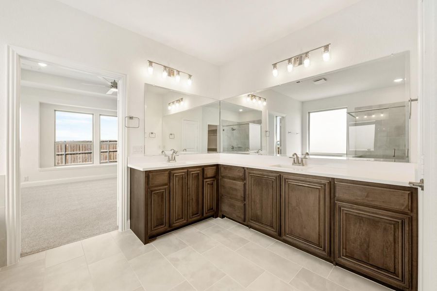 Master bathroom with L-shaped dark wood double vanity, white countertops, and large mirrors with wall lighting Master bathroom with L-shaped dark wood double vanity, white countertops, and large mirrors with wall lighting
