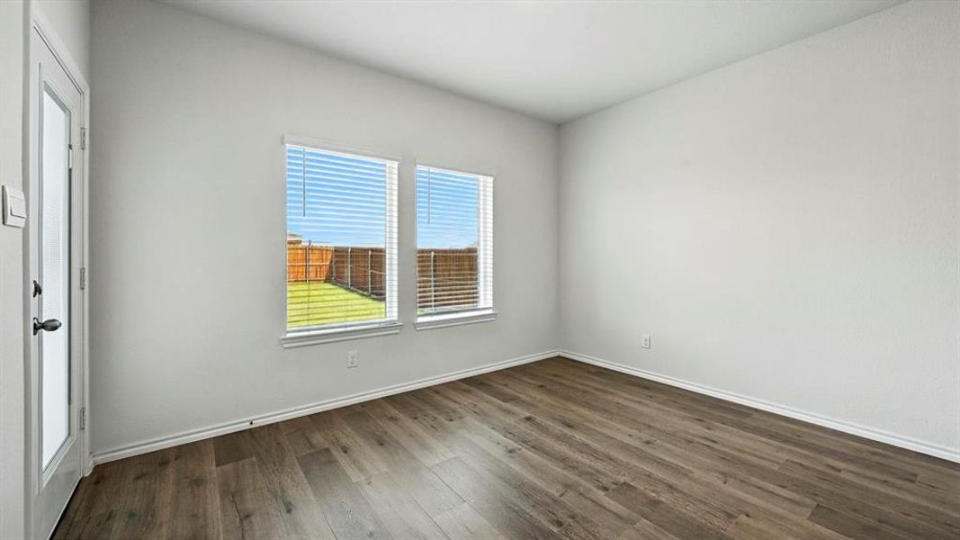 Bright interior space featuring wood-finish flooring, two large windows with blinds, a glass-paned door, and white baseboards