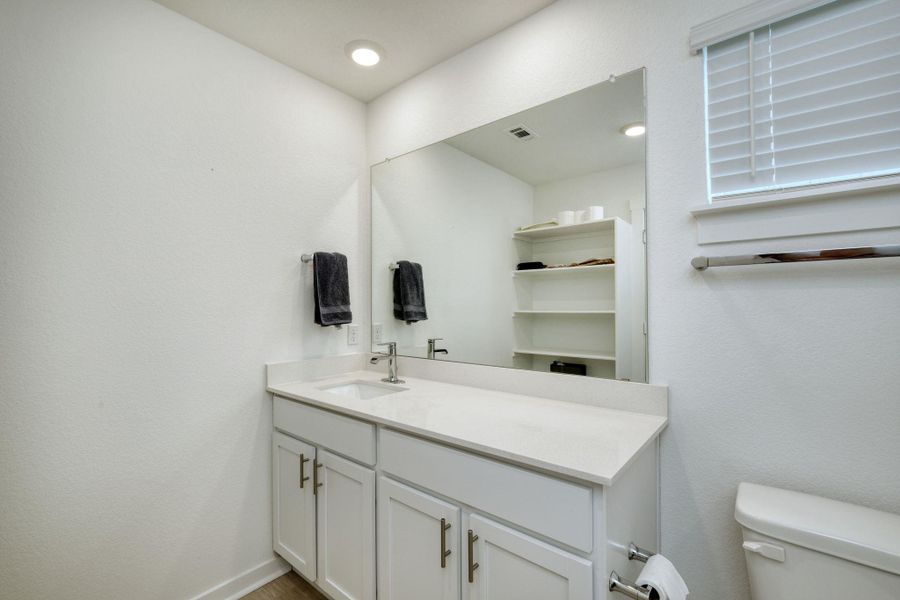 Half bath featuring toilet, baseboards, visible vents, and vanity