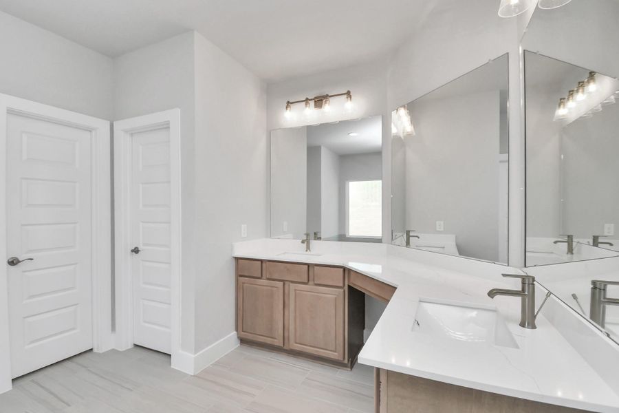 Escape to a spa-like oasis in this primary bathroom. Enjoy a walk-in shower with tile surround, a separate garden tub with custom detailing, and an elegant vanity featuring light countertops, modern hardware, and beautiful vanity lights. Experience luxury and relaxation in every detail. Sample photo of completed home with similar floor plan. Actual colors and selections may vary.