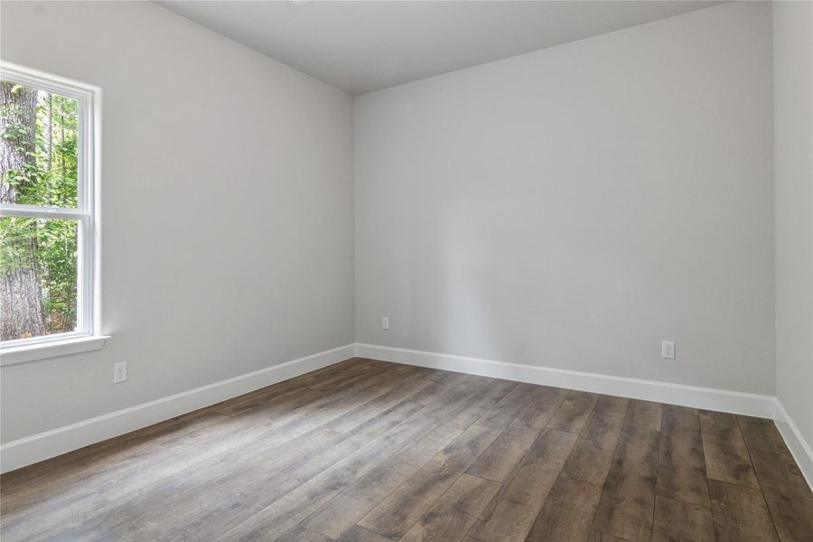 This 2nd bedroom features a bright window with a view of trees, neutral walls, and stylish LVP flooring, offering a simple and inviting space for customization.