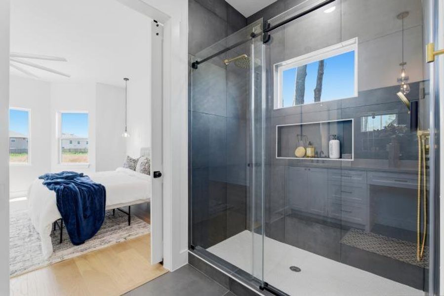 The primary bathroom offers a refined design with a glass-enclosed walk-in shower, while the right side features a double vanity, illuminated by modern pendant lighting.