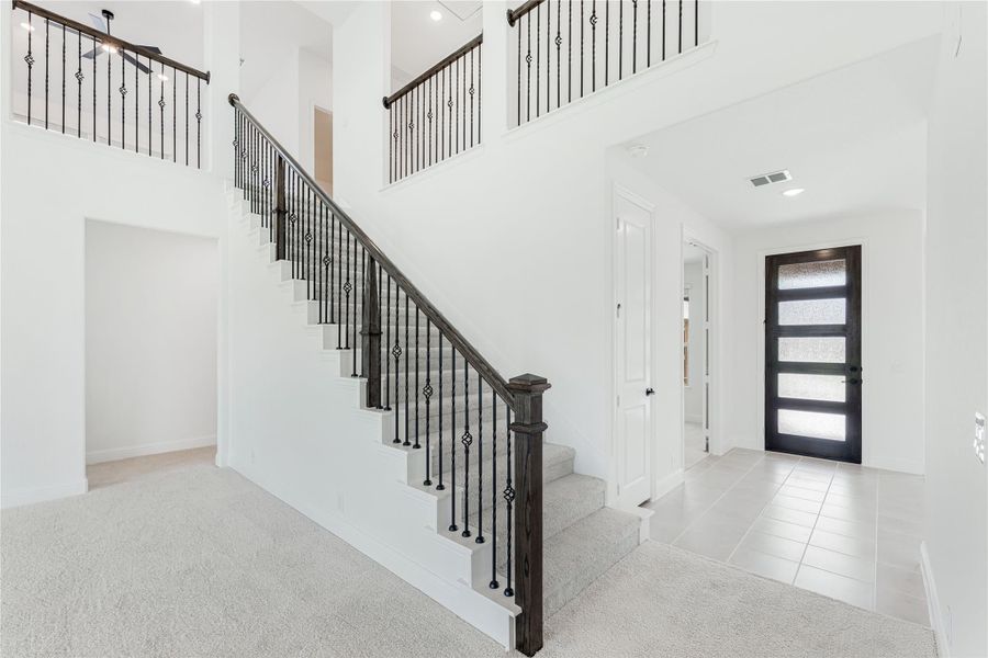 Two-story foyer with carpeted staircase, dark iron balusters, and glass-panel front door