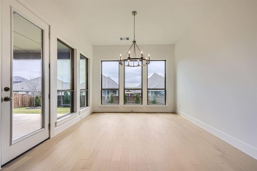 Unfurnished dining area featuring a chandelier, light wood finished floors, and baseboards