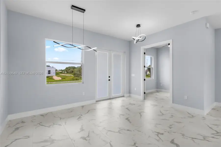 Large-format stone-finish flooring with veining detail, double-entry glass paneled doors, and contemporary sculptural overhead lighting fixtures