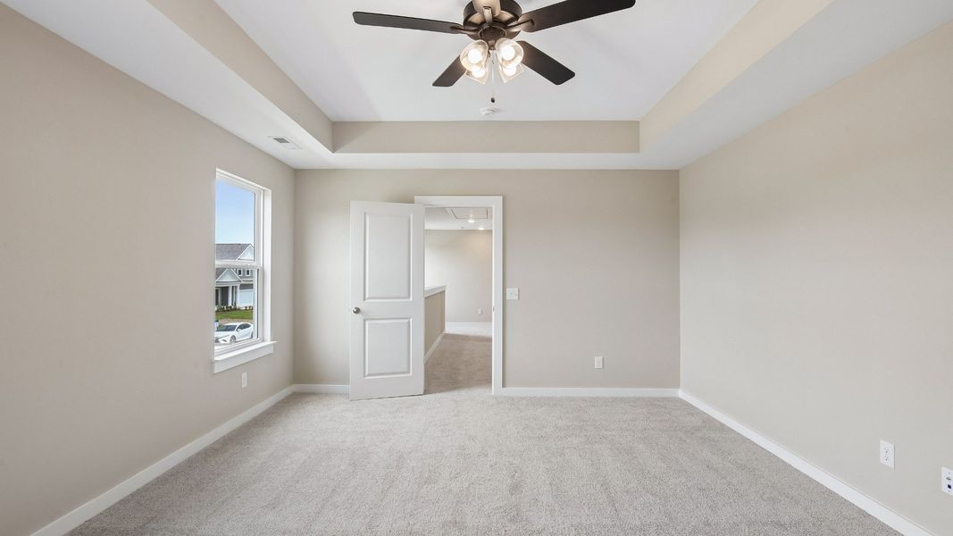 Bedroom with tray ceiling, windows, and en-suite primary bathroom