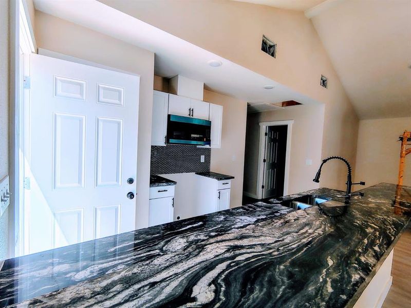 Kitchen featuring stainless steel microwave, dark stone counters, white cabinetry, wood finished floors, and high vaulted ceiling