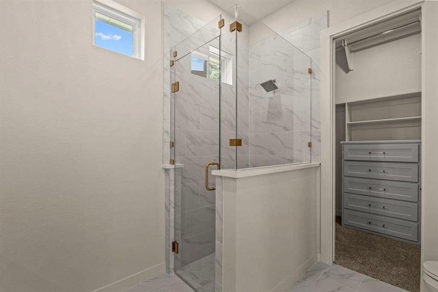 Bathroom featuring marble look tiles, plenty of natural light, and a marble finish shower