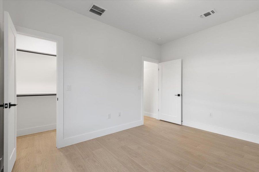 Unfurnished bedroom featuring light wood finished floors and a walk in closet Unfurnished bedroom featuring light wood finished floors and a walk in closet