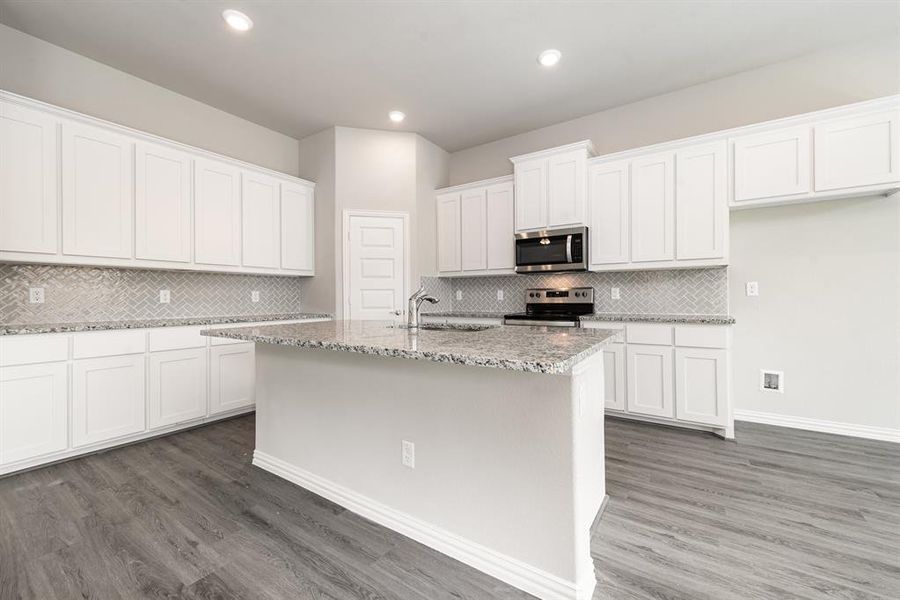 Kitchen with tasteful backsplash, white cabinets, hardwood / wood-style floors, appliances with stainless steel finishes, and sink