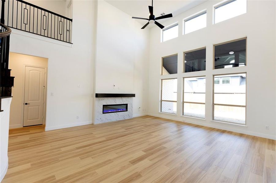 Unfurnished living room featuring a towering ceiling, a high end fireplace, light hardwood / wood-style floors, and ceiling fan