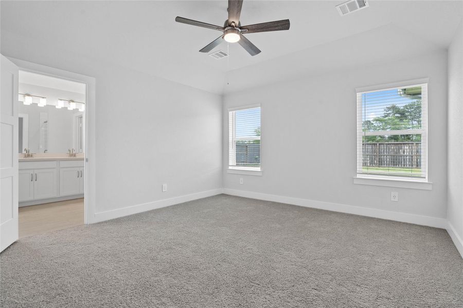 The primary bedroom provides a peaceful escape with a bright, neutral palette, sloped ceilings, ceiling fan, large windows (fitted with blinds), and plush carpet flooring, creating a calm and restorative atmosphere to end your day.