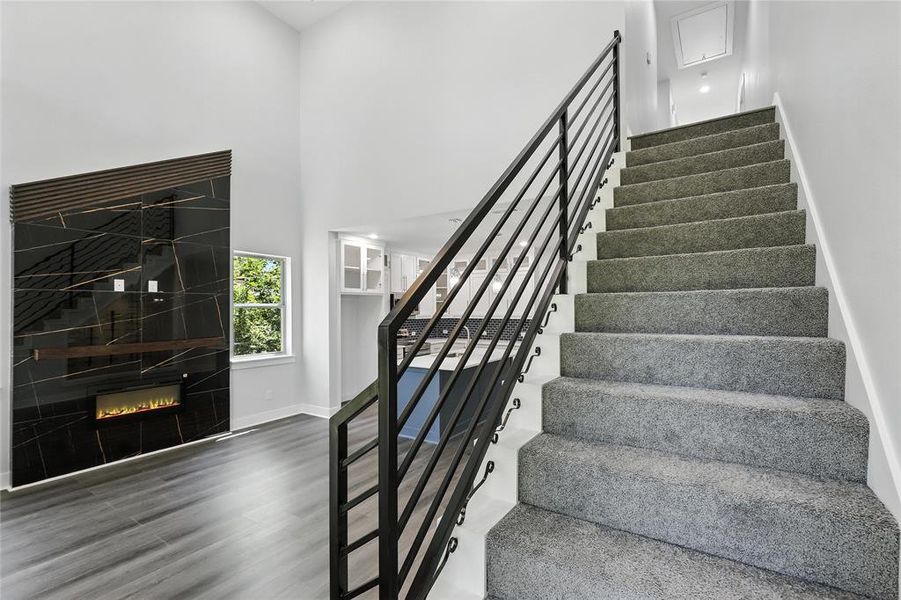 Staircase with a high ceiling, a glass covered fireplace, and wood finished floors