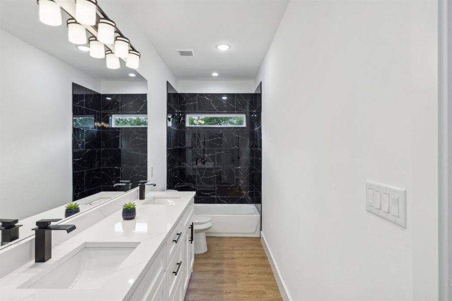 Full bathroom featuring tiled shower / bath combo, toilet, wood-type flooring, and double vanity