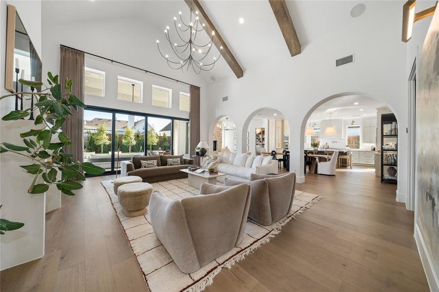 Living room featuring light hardwood / wood-style floors, a towering ceiling, beam ceiling, and an inviting chandelier