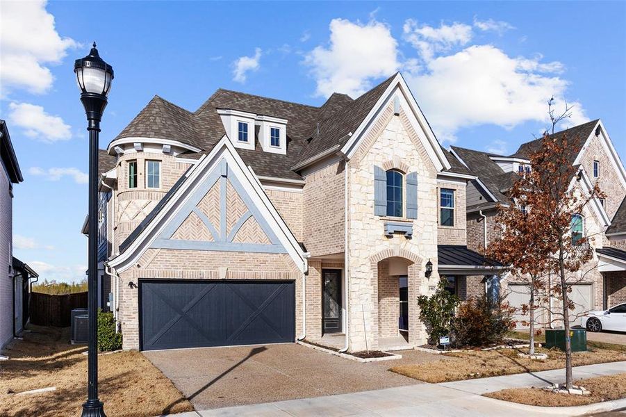 French country style house with stone siding, a shingled roof, driveway, brick siding, and an attached garage