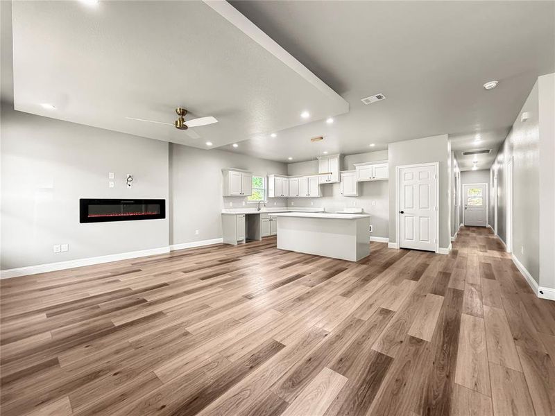 Open-concept living area featuring wood-finish flooring, a wall-mounted electric fireplace, recessed lighting, and a contemporary ceiling fan