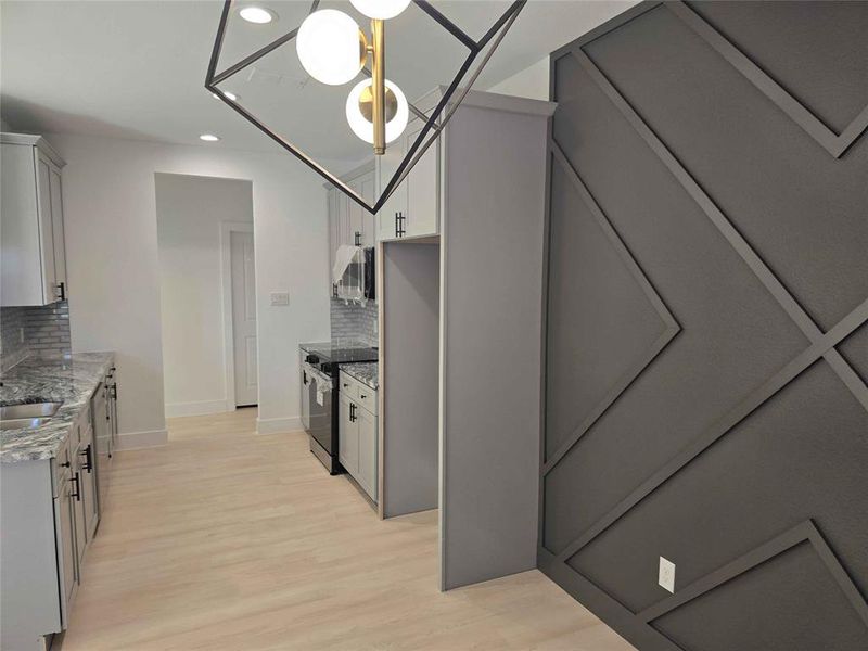 Kitchen featuring light  laminate flooring, backsplash, custom granite counters, stainless steel range with 5 burner stovetop, under cabinet lighting