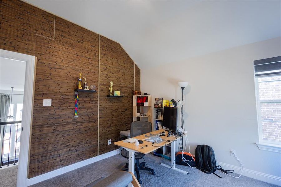 Carpeted office with lofted ceiling and wooden walls