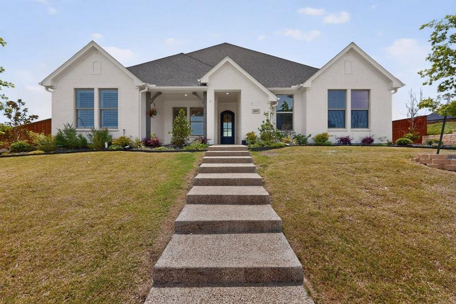 White brick exterior with a dark gray shingled roof, featuring a covered entry with exposed wood-look beams White brick exterior with a dark gray shingled roof, featuring a covered entry with exposed wood-look beams