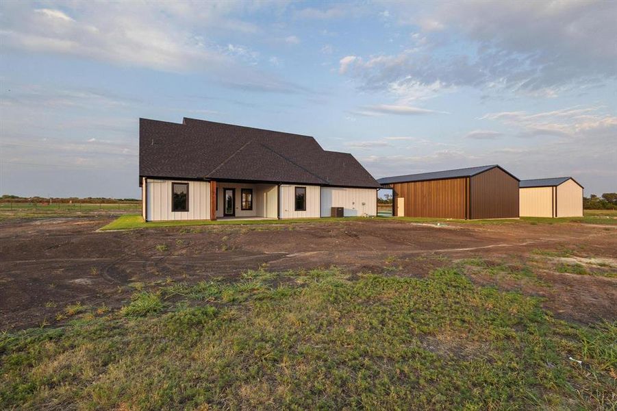 Modern farmhouse style home featuring an outdoor structure, an outbuilding, a patio area, and a shingled roof