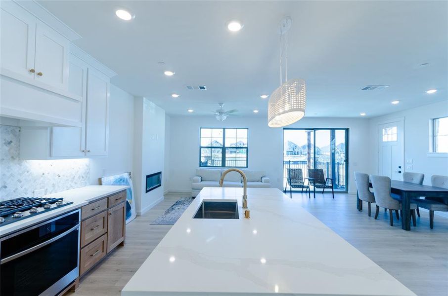 Kitchen featuring stainless steel appliances, an island with sink, light wood-style floors, light stone counters, and tasteful backsplash