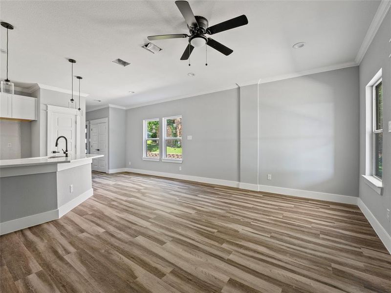 Unfurnished living room featuring ornamental molding, a ceiling fan, light wood-type flooring, baseboards, and a sink