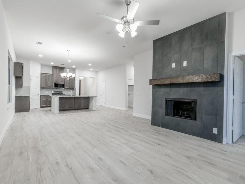 Unfurnished living room with ceiling fan with notable chandelier, sink, light hardwood / wood-style floors, and a tile fireplace