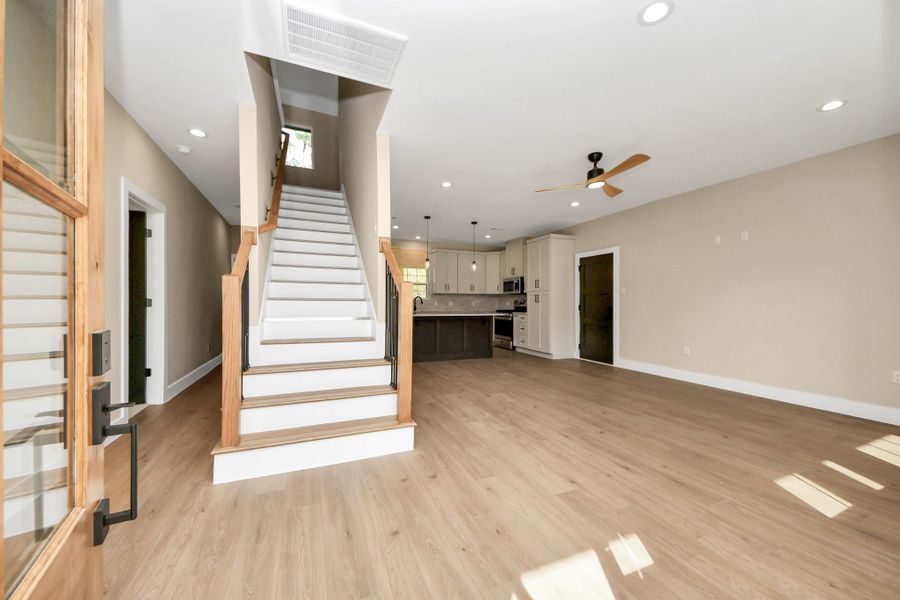 Greeted by an elegant glass front door, you’re welcomed into a bright open-concept living space featuring luxury vinyl plank flooring, recessed lighting, and a modern staircase with wood accents. The layout flows seamlessly into the kitchen area, creating the perfect space for everyday living and entertaining.