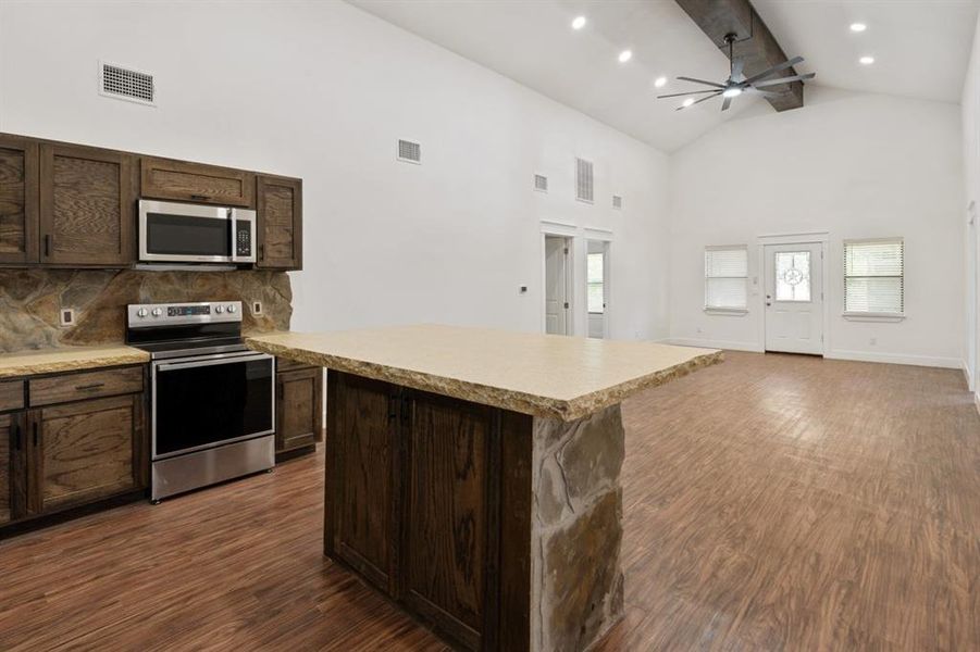 Kitchen with dark wood-type flooring, high vaulted ceiling, stainless steel appliances, a center island, and ceiling fan