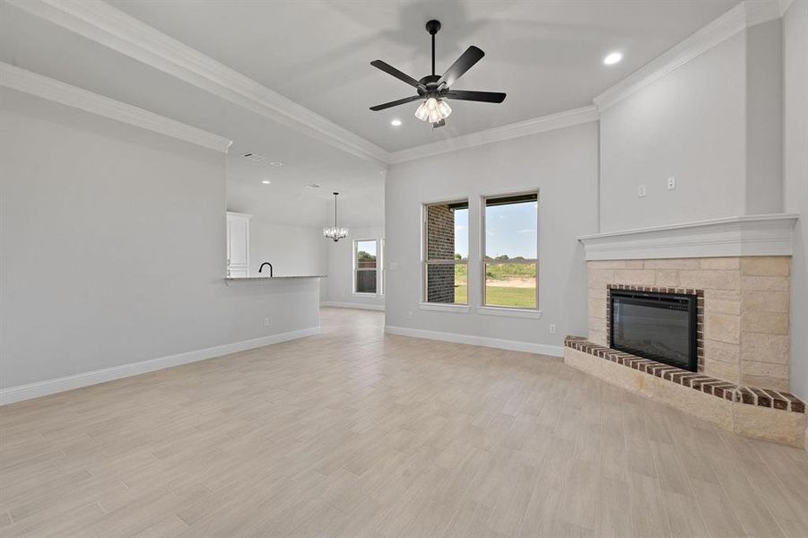 Unfurnished living room with ceiling fan, light wood-type flooring, a glass covered fireplace, crown molding, and suspended lighting