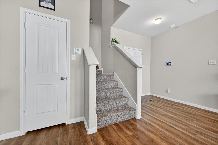 This photo features a modern, well-lit entryway with hardwood flooring and carpeted stairs leading to an upper level. Neutral wall colors and a clean design create a welcoming atmosphere.