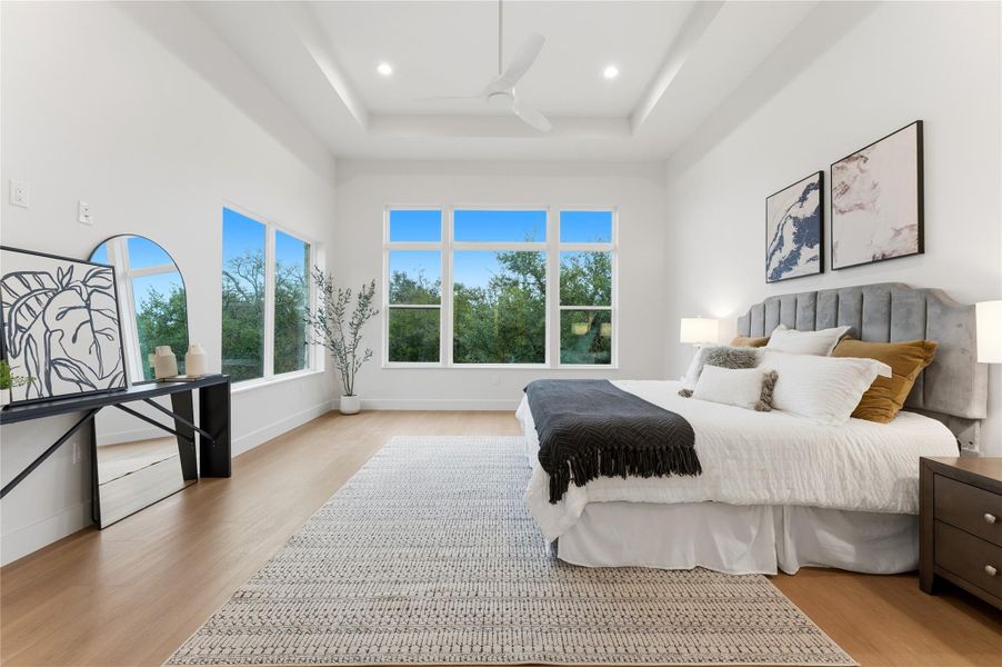 Bedroom with light wood finished floors, a ceiling fan, a raised ceiling, a high ceiling, and recessed lighting