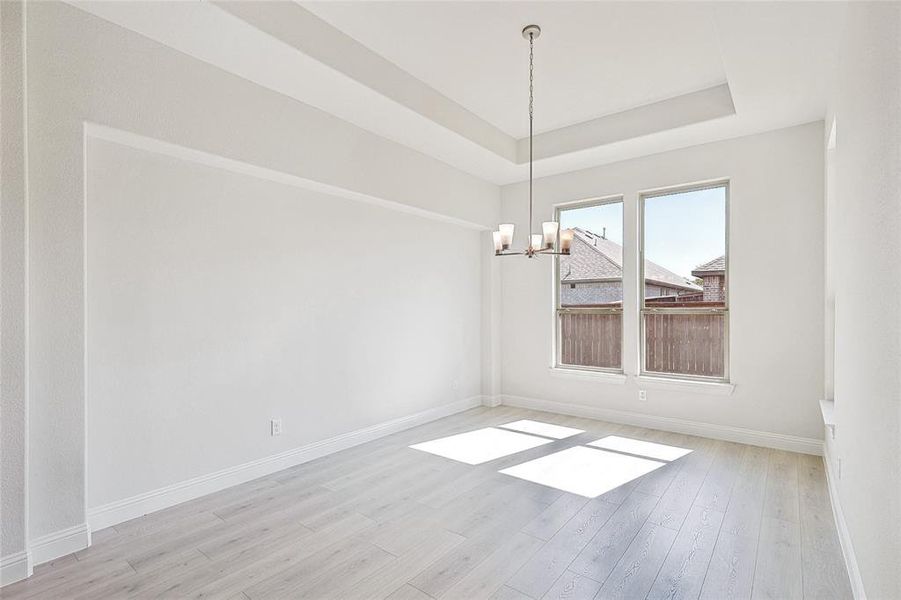 Unfurnished dining area featuring light hardwood / wood-style floors, a notable chandelier, and a tray ceiling