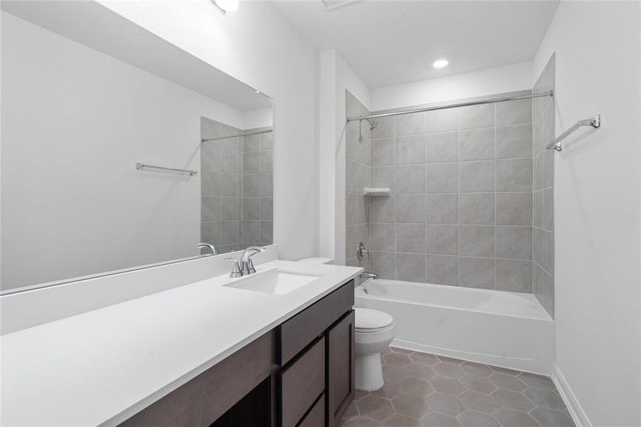 Secondary bath features tile flooring, bath/shower combo with tile surround, stained wood cabinets, beautiful light countertops, mirror, sleek fixtures and modern finishes.