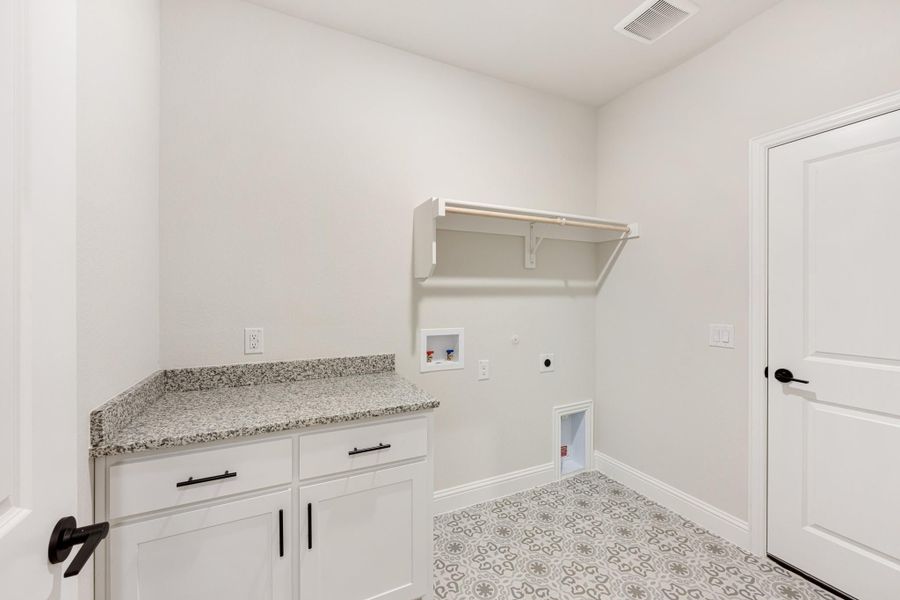 Laundry room with white cabinets, granite countertop, wall shelf, and patterned tile floor Laundry room with white cabinets, granite countertop, wall shelf, and patterned tile floor