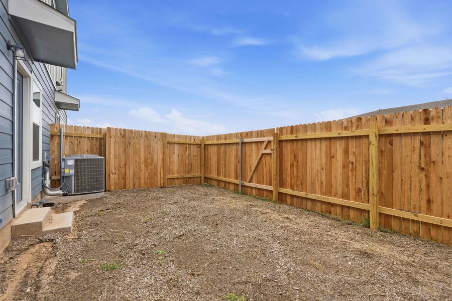 Fenced backyard featuring a wood privacy fence with gate, exterior siding, and a concrete step leading to an exterior door Fenced backyard featuring a wood privacy fence with gate, exterior siding, and a concrete step leading to an exterior door
