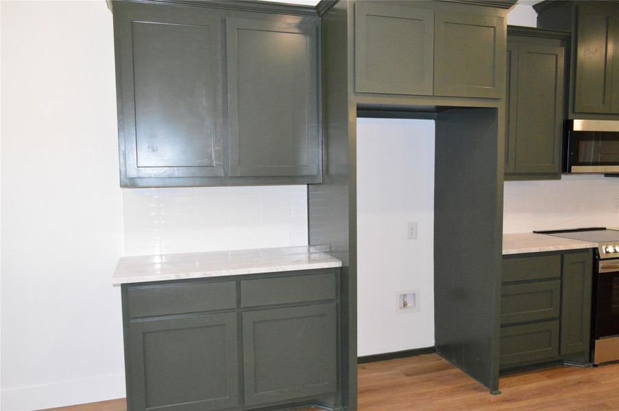 Kitchen featuring stainless steel appliances, decorative backsplash, light wood finished floors, and green cabinetry Kitchen featuring stainless steel appliances, decorative backsplash, light wood finished floors, and green cabinetry