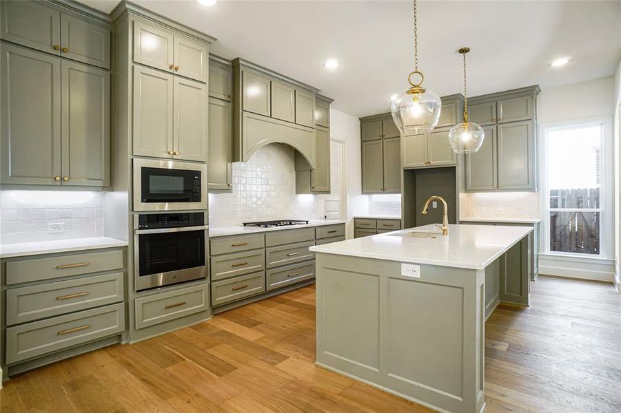 Kitchen with decorative light fixtures, stainless steel appliances, tasteful backsplash, a center island with sink, and recessed lighting