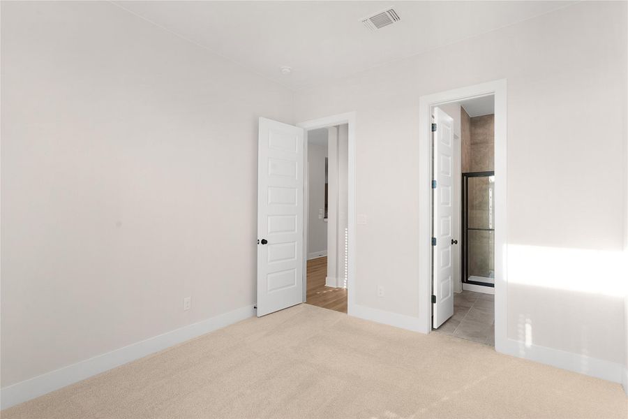 A well-lit bedroom features plush carpeting and convenient access to a private bathroom with a glass-enclosed shower. A well-lit bedroom features plush carpeting and convenient access to a private bathroom with a glass-enclosed shower.