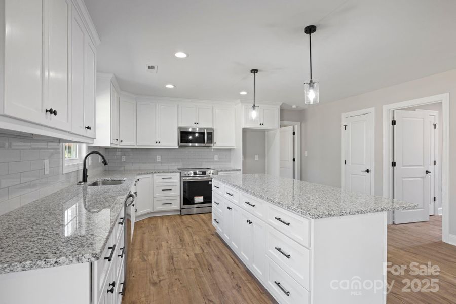 Bright, modern kitchen with white cabinetry, gleaming granite countertops, subway tile backsplash, and stylish pendant lighting—offering ample workspace and storage. Bright, modern kitchen with white cabinetry, gleaming granite countertops, subway tile backsplash, and stylish pendant lighting—offering ample workspace and storage.