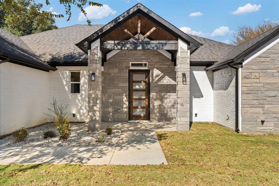 Property entrance with a shingled roof, a yard, and stone siding