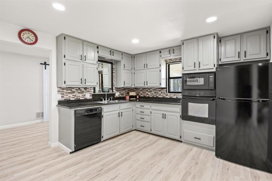 Kitchen featuring black appliances, light hardwood / wood-style flooring, tasteful backsplash, sink, and gray cabinets