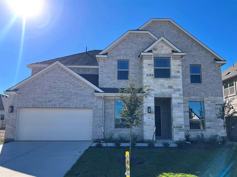 View of front facade with driveway, a garage, a front lawn, brick siding, and stone siding