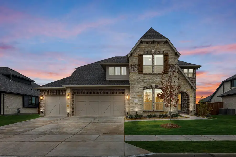 Two-story stone and brick home with three-car garage, arched entry, and manicured front lawn at dusk Two-story stone and brick home with three-car garage, arched entry, and manicured front lawn at dusk