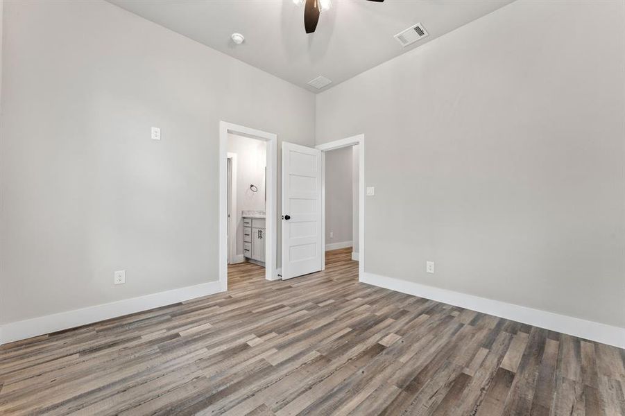 Unfurnished bedroom with ensuite bath, wood-type flooring, and ceiling fan