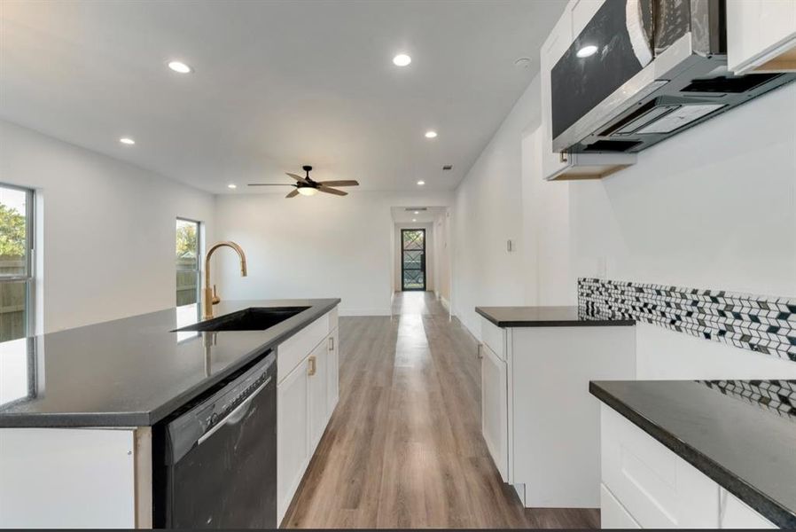 Kitchen featuring white cabinetry, stainless steel dishwasher, sink, and an island with sink